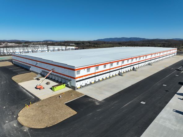 A 251,000 square foot warehouse is in the final stages of construction. The building is white except for two horizontal orange stripes, and there is a large number of truck dock doors on the building for deliveries